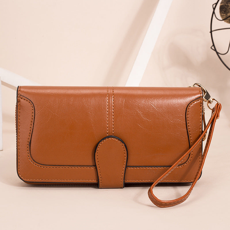 Brown leather clutch bag with a strap on a beige background