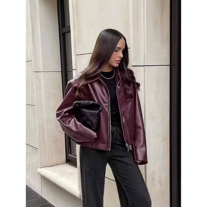 Woman wearing a burgundy leather jacket with black fur lining, standing against a neutral wall.
