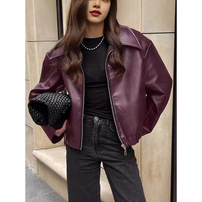 Person wearing a purple leather jacket and black outfit, holding a black handbag.