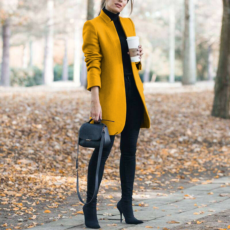 Woman in a yellow coat holding a coffee cup in an autumn setting