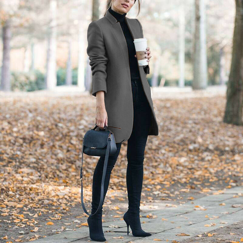 Woman in a long coat holding a coffee cup in an outdoor setting with autumn leaves.