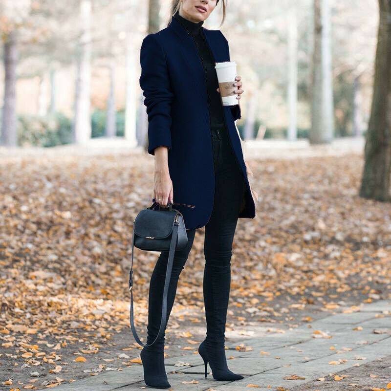 Woman in navy coat and black outfit holding a coffee cup in an autumn park.