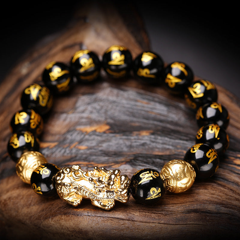 Black and gold beaded bracelet with a dragon clasp on a wooden surface