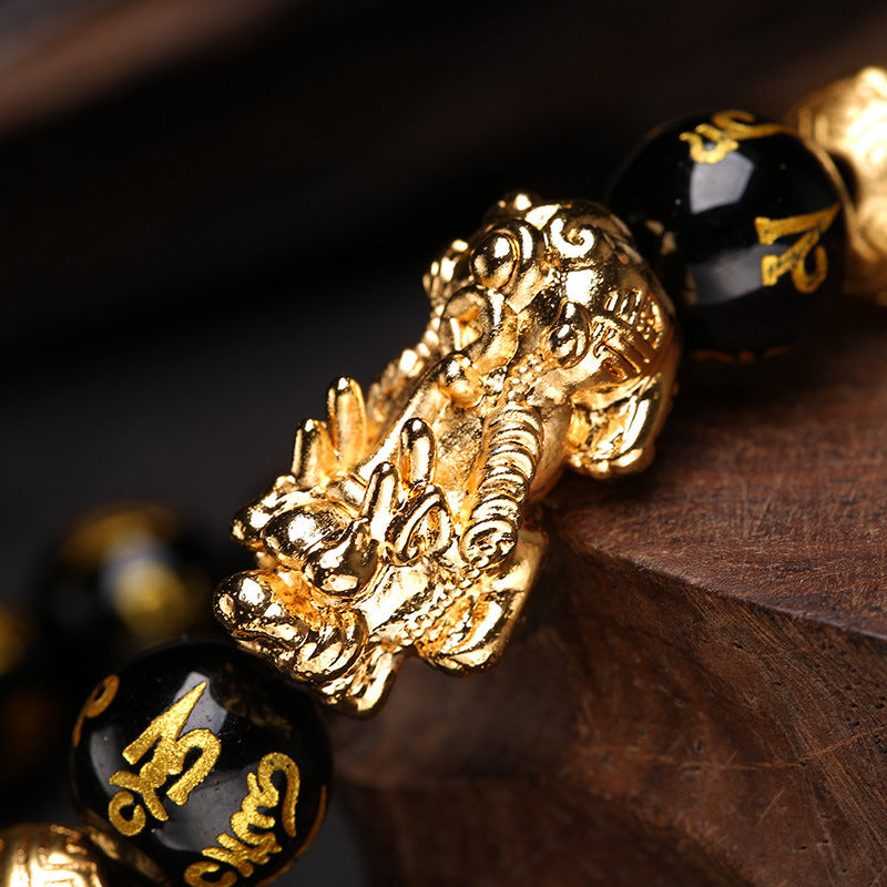 Close-up of a gold dragon pendant on black beads with gold text, on a dark background.