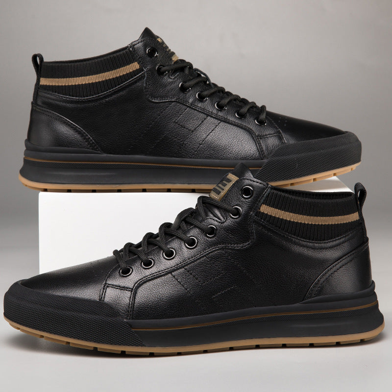A pair of black leather mid-top sneakers with black laces, black ribbed ankle cuffs, and a tan outsole, displayed on a white block against a gray background.