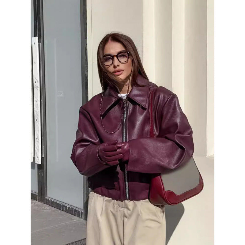 Woman wearing a burgundy leather jacket and holding a matching handbag against a neutral background.
