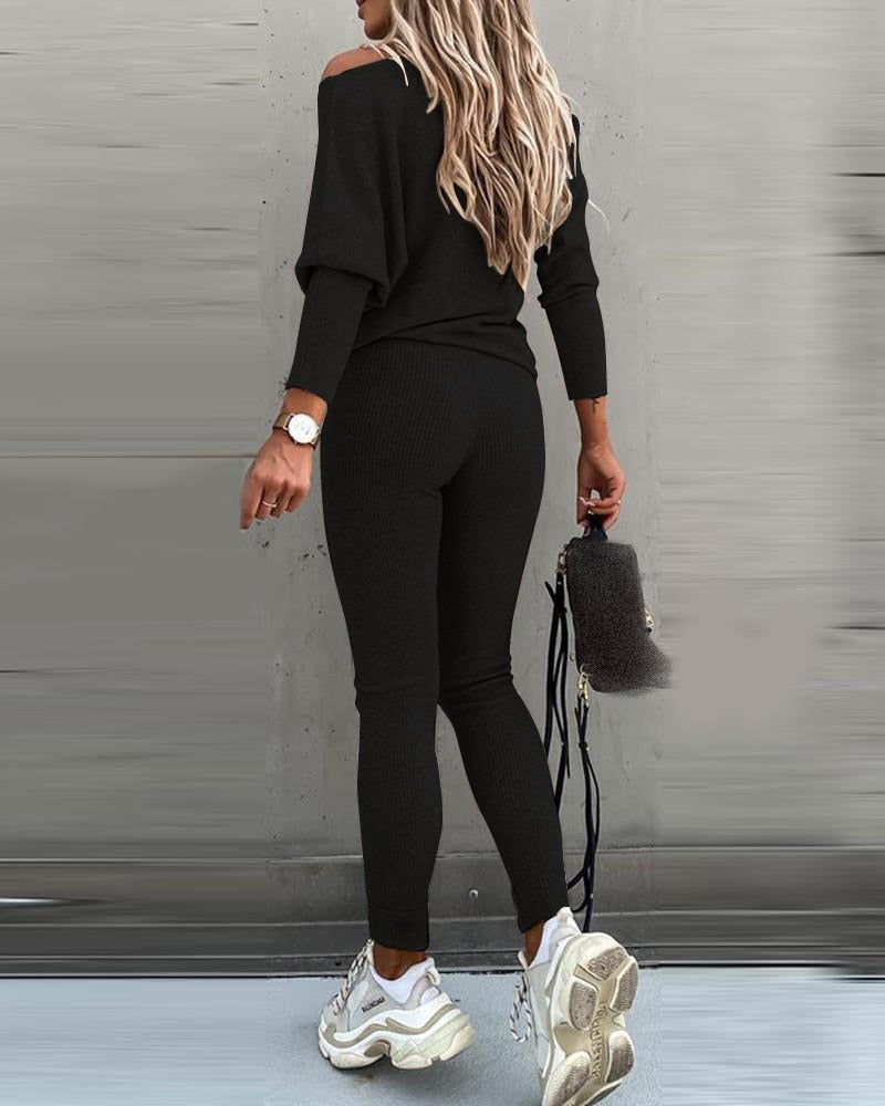 Person wearing a black outfit with white sneakers against a gray wall.