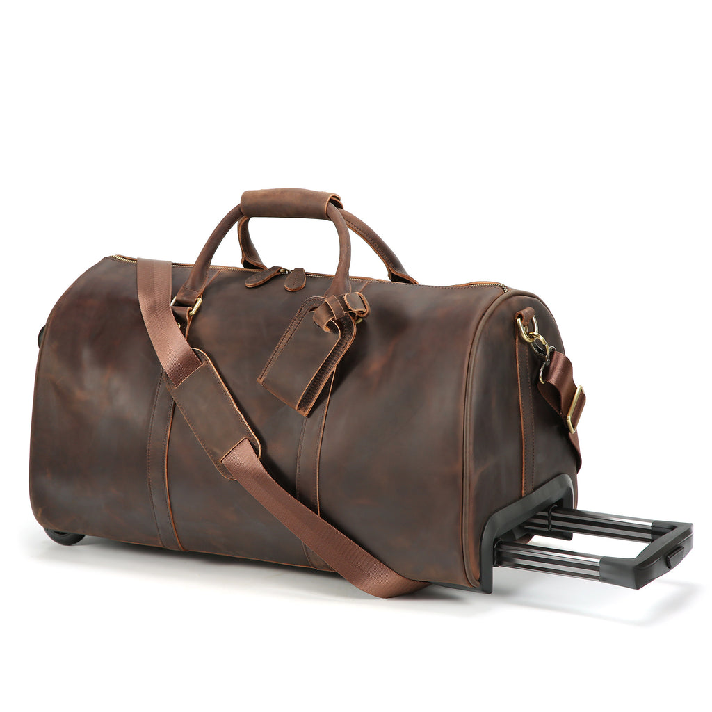 A dark brown distressed leather duffel bag with a telescoping rolling handle extended, featuring dual top handles, a detachable shoulder strap, and a small leather luggage tag, shown on a white background.