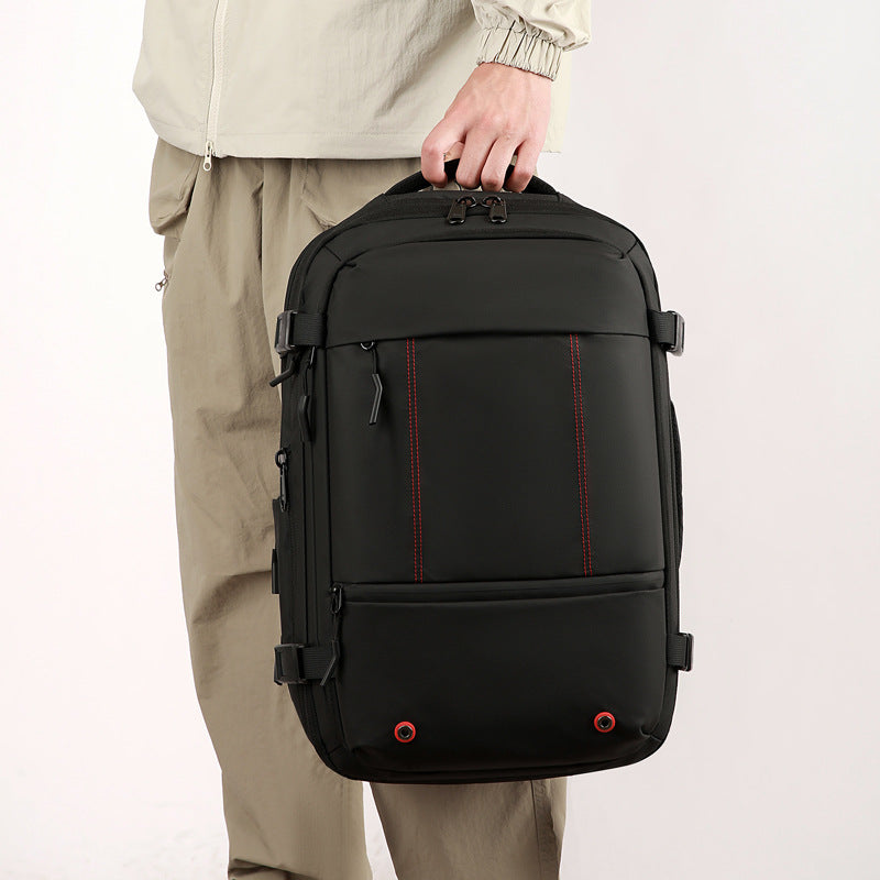A person wearing beige pants and a light-colored jacket holds a black laptop backpack with red contrast stitching. The backpack features multiple zippered compartments and side compression straps, shown against a plain light background.