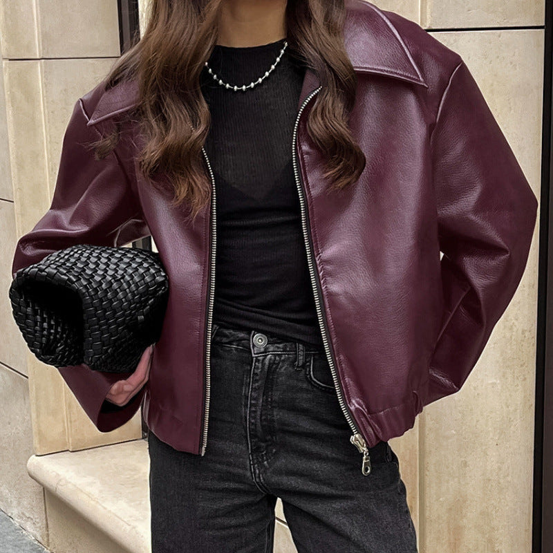 Person wearing a burgundy leather jacket and black outfit holding a black textured bag.