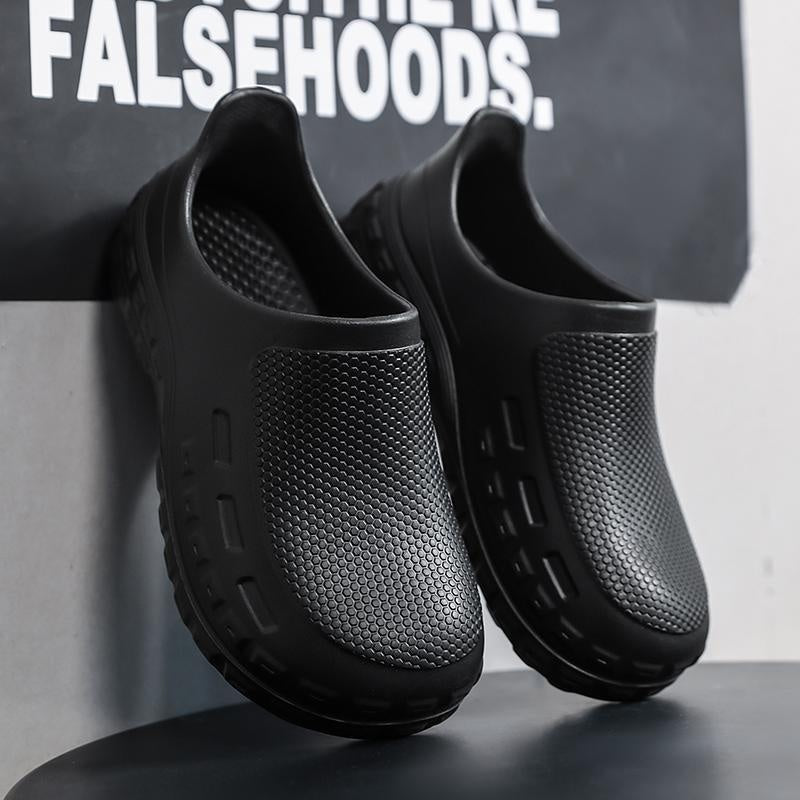A pair of black slip-on clogs with textured perforated uppers and chunky soles, leaning against a dark wall with bold white text in the background.