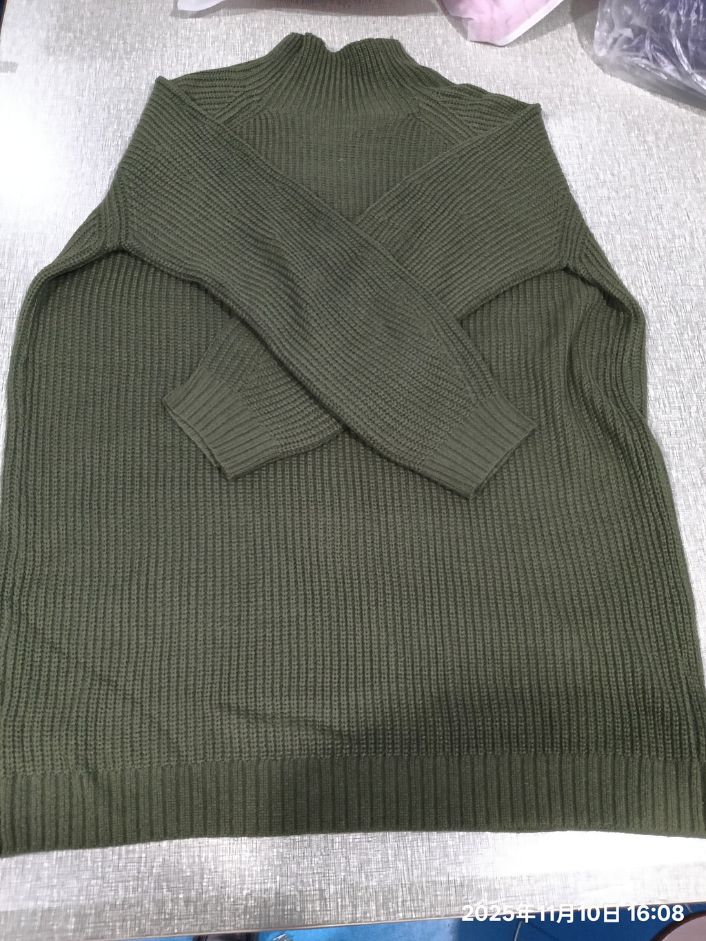 An olive green ribbed knit mock-neck sweater laid flat on a light gray fabric surface.