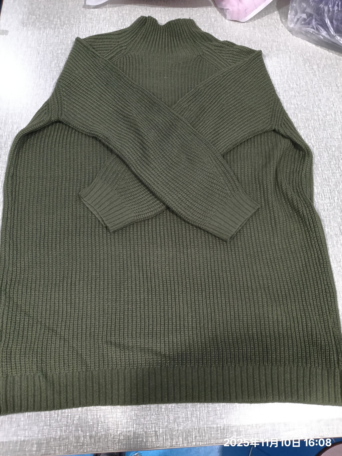 An olive green ribbed knit mock-neck sweater laid flat on a light gray fabric surface.