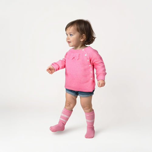 Child wearing a pink sweater, shorts, and pink knee-high socks on a white background