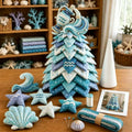 A handmade fabric Christmas tree ornament made of layered star and wave shapes in shades of blue, teal, and white, displayed on a wooden table with matching starfish and shell ornaments, a cone-shaped white object, and a small printed photo in a home decor setting.