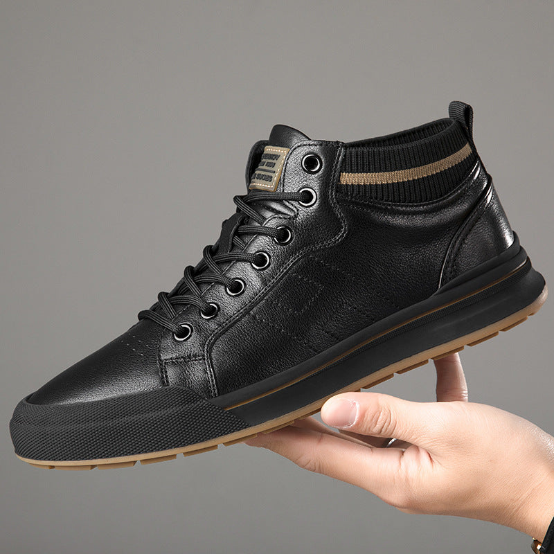 A black leather mid-top sneaker with a ribbed black ankle collar, held by a hand against a solid gray background.