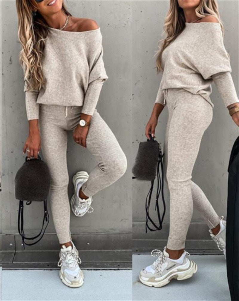 Woman wearing a gray off-shoulder top and leggings with sneakers, holding a black bag.