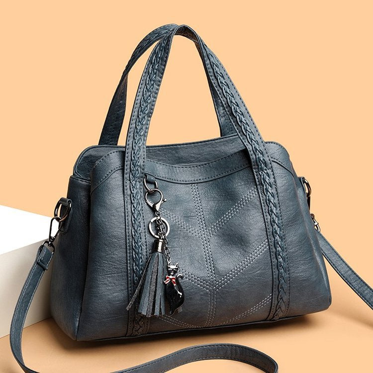 Blue handbag with braided handle and tassel on a beige background