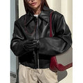 Person wearing a black leather jacket with a red interior, standing against a light-colored wall.