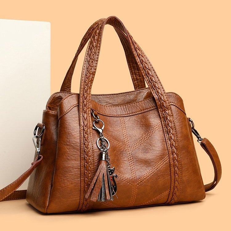 Brown leather handbag with braided handle and tassel on a beige background