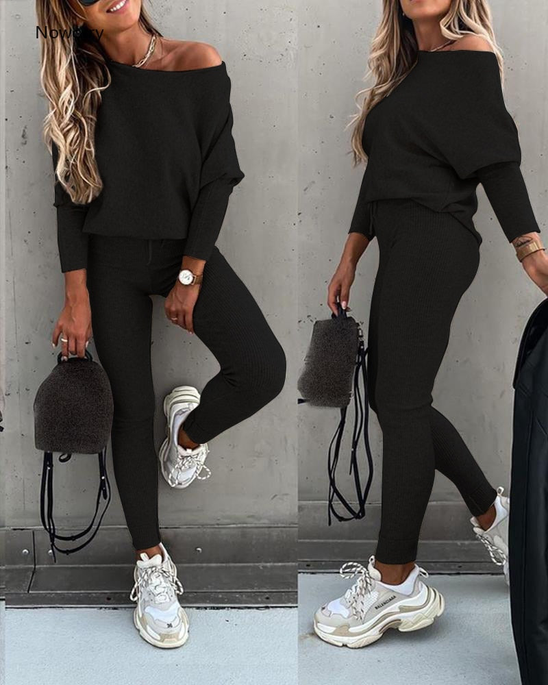 Woman wearing a black off-shoulder top and leggings with white sneakers, holding a small black bag.