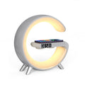 A modern C-shaped desk lamp with a built-in phone charger and digital alarm clock, featuring a warm yellow LED light glow and a silver-gray body on a white background.