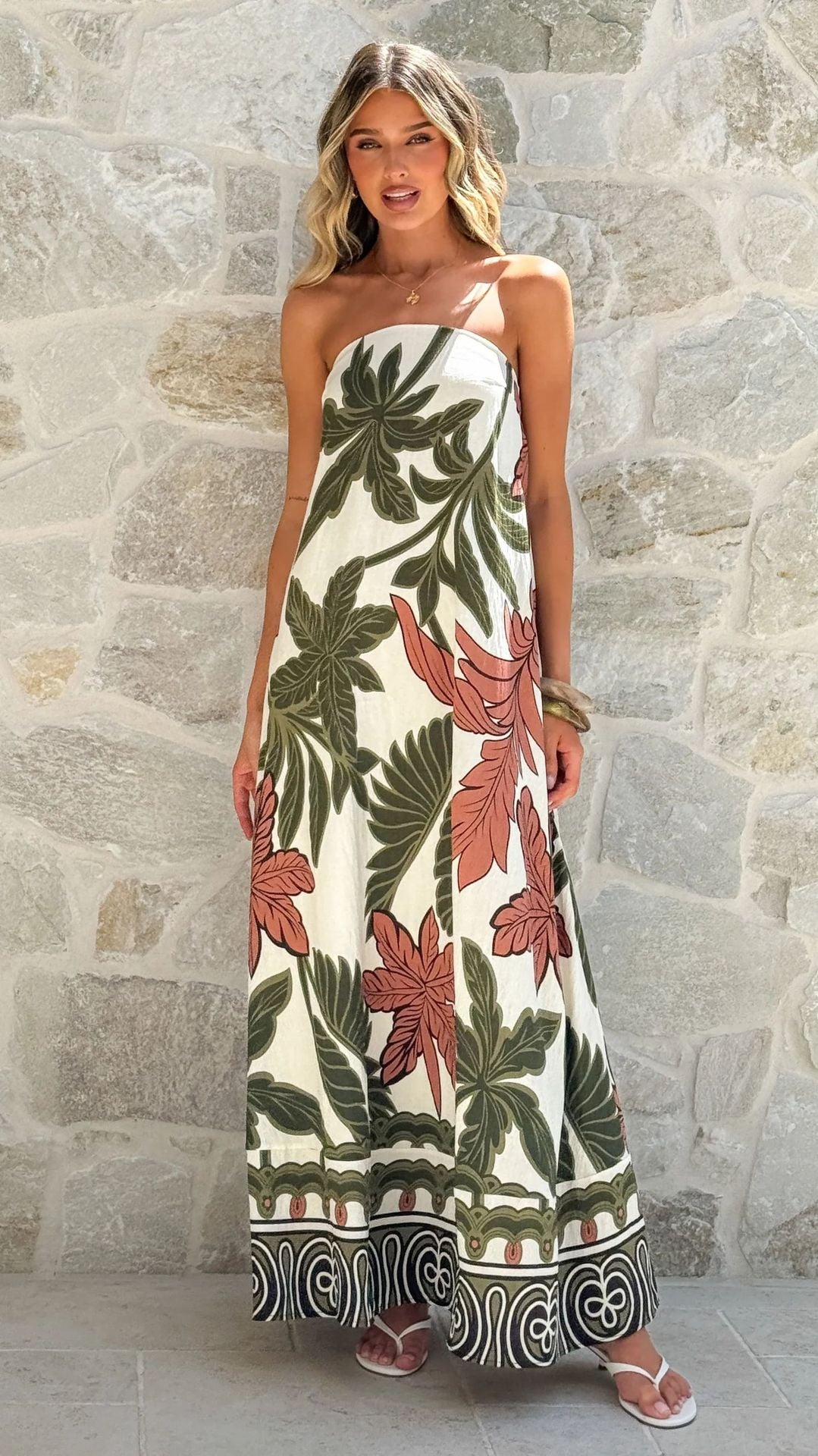 Woman wearing a strapless floral dress against a stone wall.