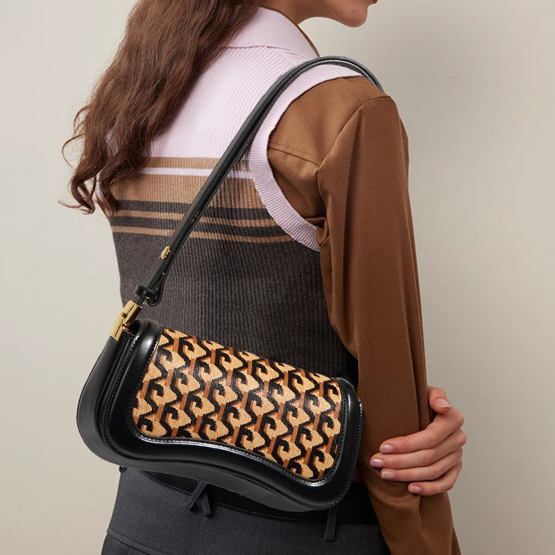 A woman wearing a brown and gray striped sweater vest over a light pink top, carrying a black shoulder bag with a tan and black Goyardine monogram patterned flap.