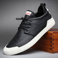 A black leather casual sneaker with a white rubber sole, resting on a wooden box against a gray studio background. The brand name 'booda' is visible on the tongue label.