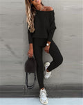 Woman in black off-shoulder top and leggings with white sneakers against a gray wall.