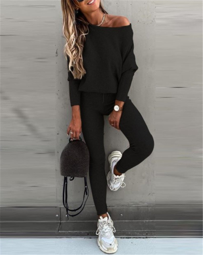Woman in black off-shoulder top and leggings with white sneakers against a gray wall.