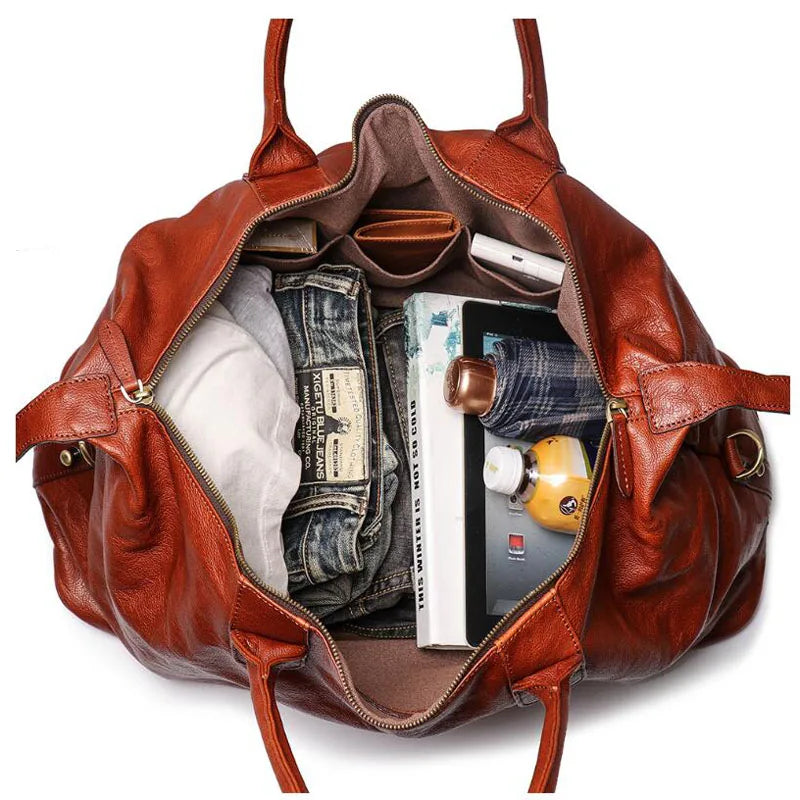 An open brown leather duffel bag shown from above, filled with travel items including folded jeans, a white shirt, a tablet, a book, and a small bottle, on a white background.