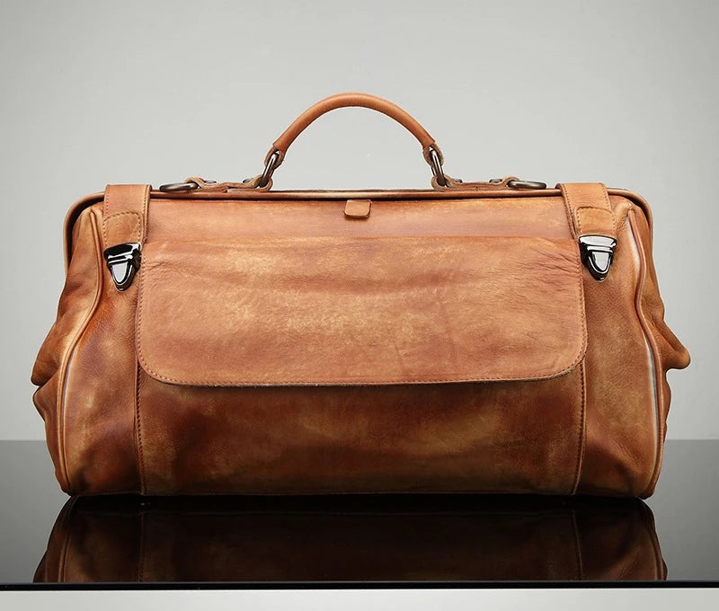 Brown leather duffel bag on a reflective surface with a gray background