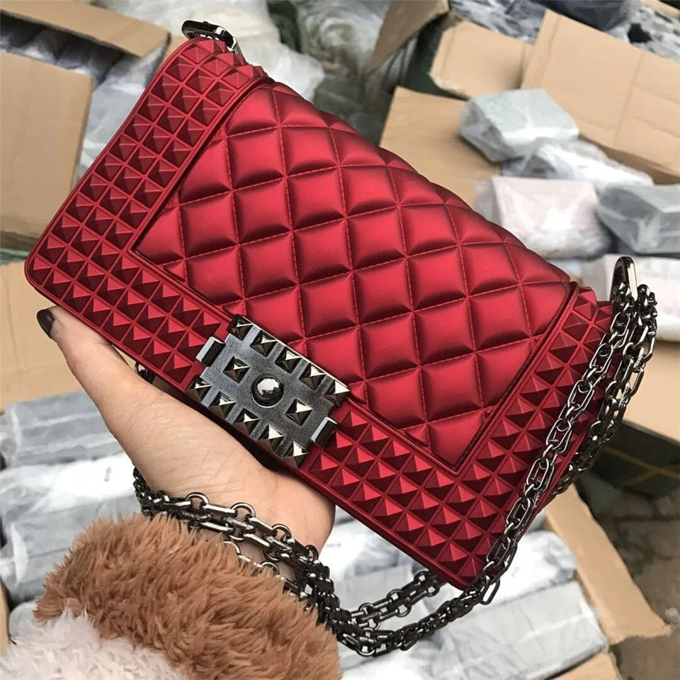 Red quilted handbag with chain strap held by a person against a blurred background