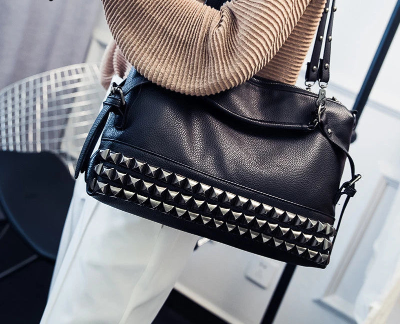 Black studded handbag held by a person wearing a beige sweater.