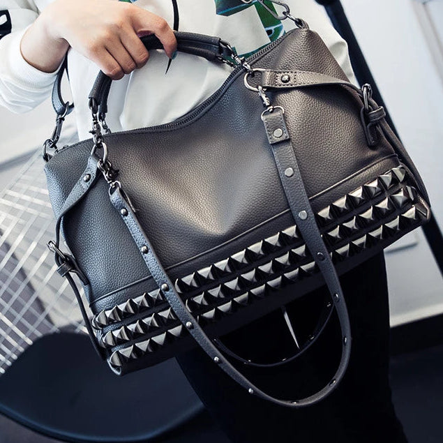 Person holding a black studded handbag with a blurred indoor background