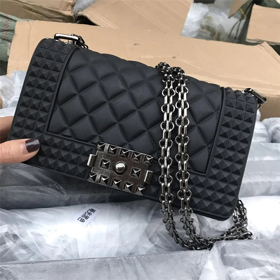 Black quilted handbag with chain strap held by a hand on a gray surface.