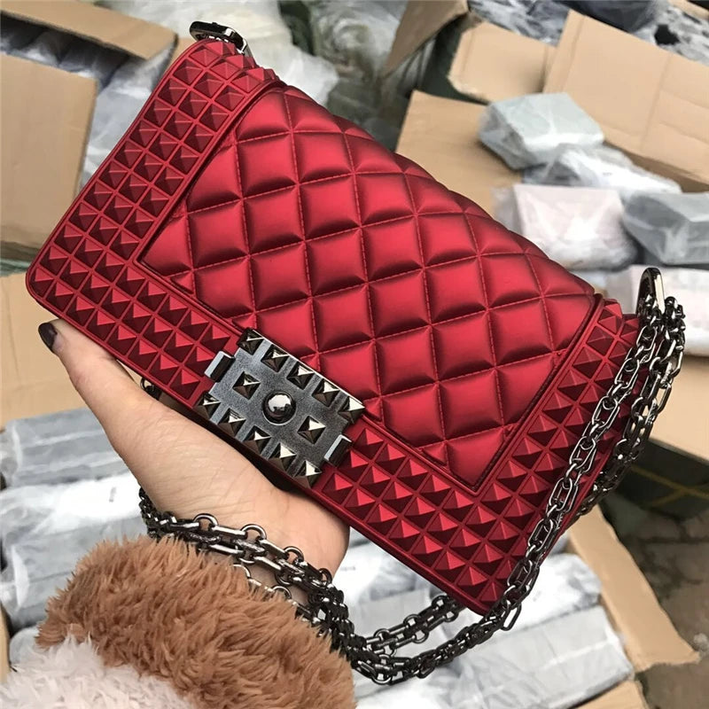 Red quilted handbag with chain strap held by a person against a blurred background