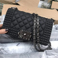 Black quilted handbag with chain strap held by a hand against a cardboard box background