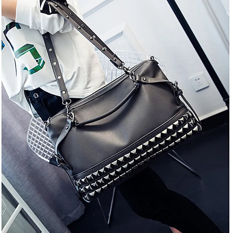 Black studded handbag held by a person wearing a white shirt with green text.