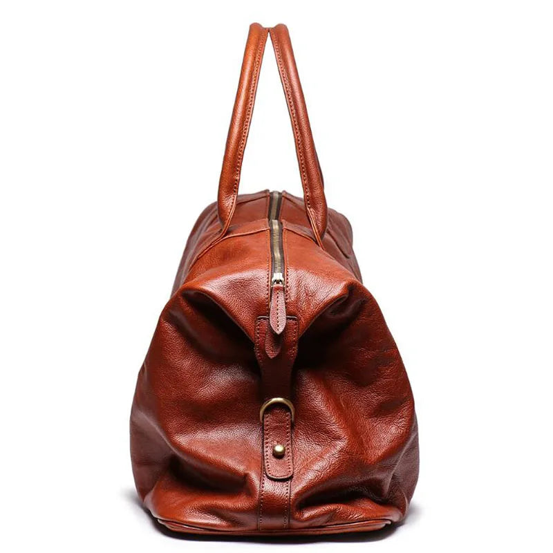 A brown leather duffel bag with dual top handles, a front zipper closure, and a brass-tone buckle detail, shown against a plain white background.