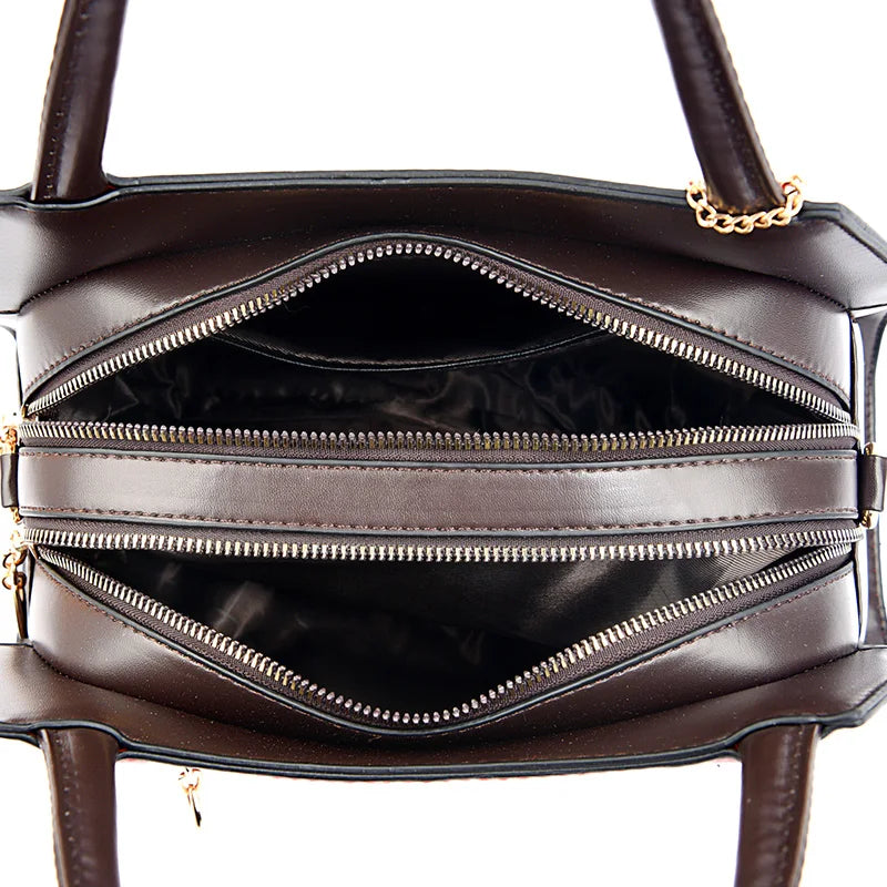 Brown leather handbag with gold zipper and chain detail on a white background