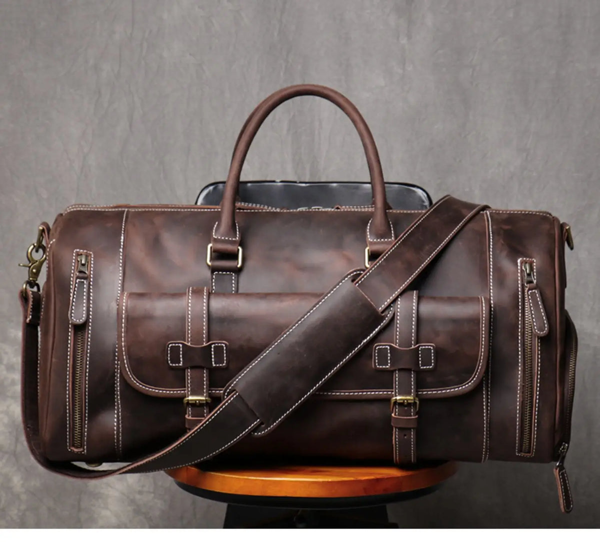Brown leather duffel bag with a shoulder strap on a gray background
