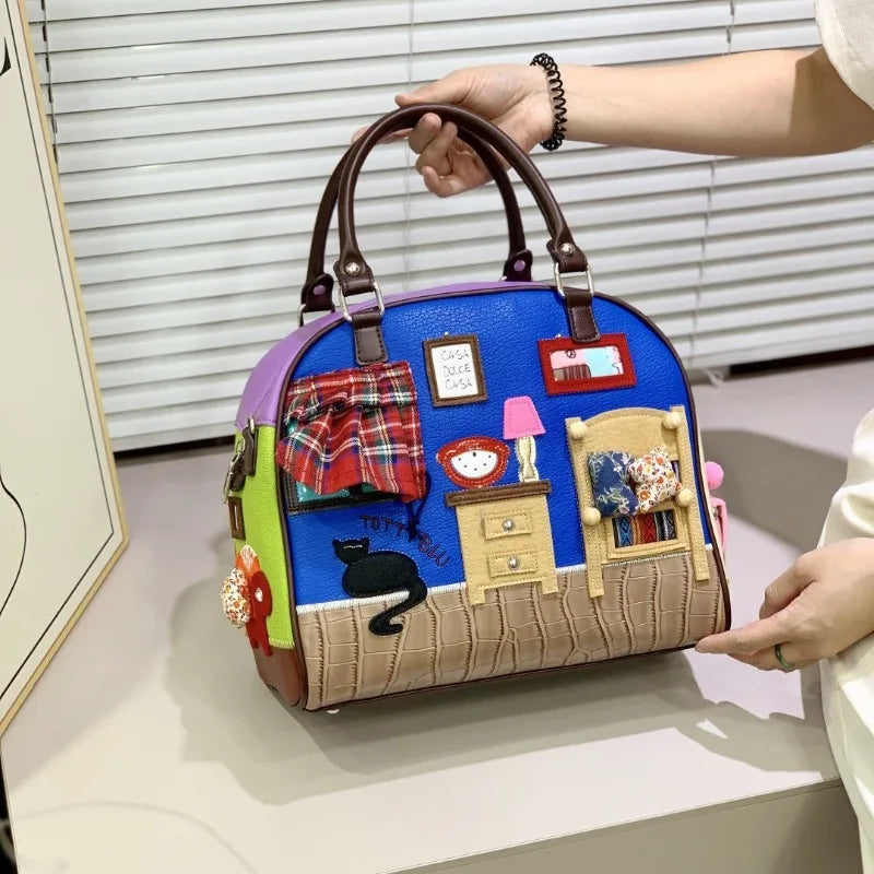 Colorful handbag with miniature scenes and a black cat design, held by a person.