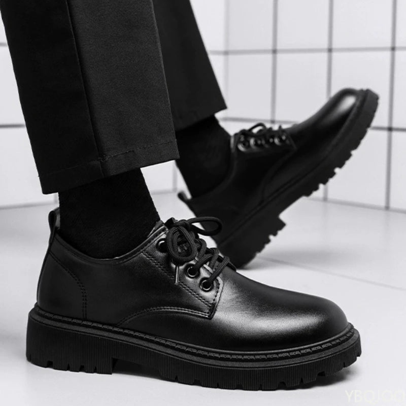 Black leather shoes worn with black pants on a white floor.