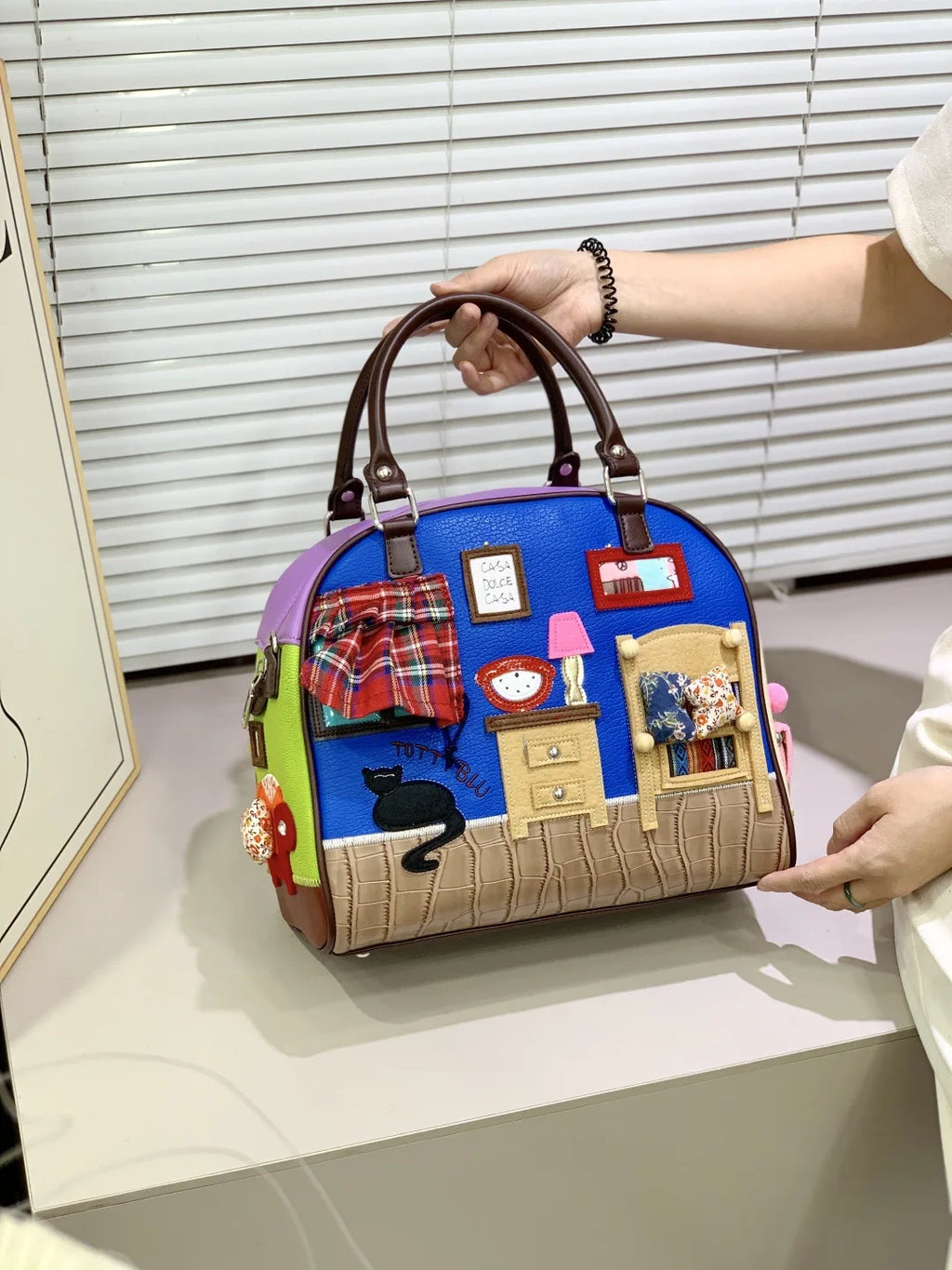 Colorful handbag with a room-themed design held by a person.