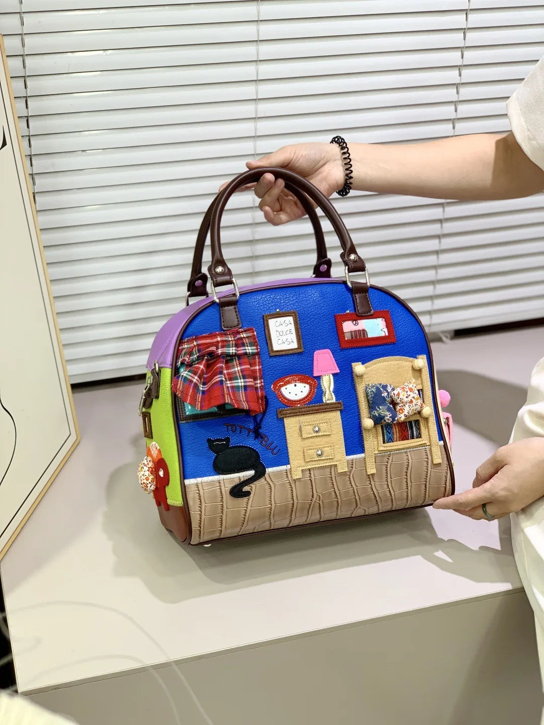 Colorful handbag with a room-themed design held by a person.