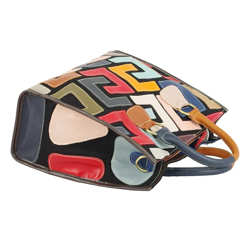 A structured leather handbag with a colorful geometric patchwork design, featuring dark blue, red, yellow, beige, and light blue sections, with tan leather handles on a white background.