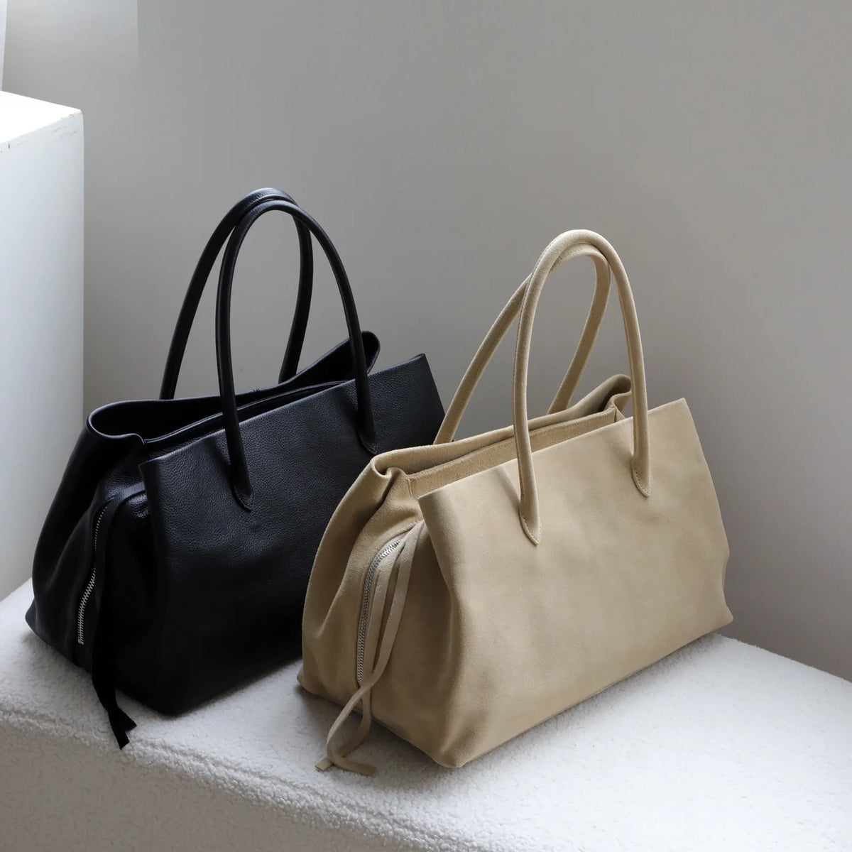 Black and beige handbags on a white surface with a neutral background