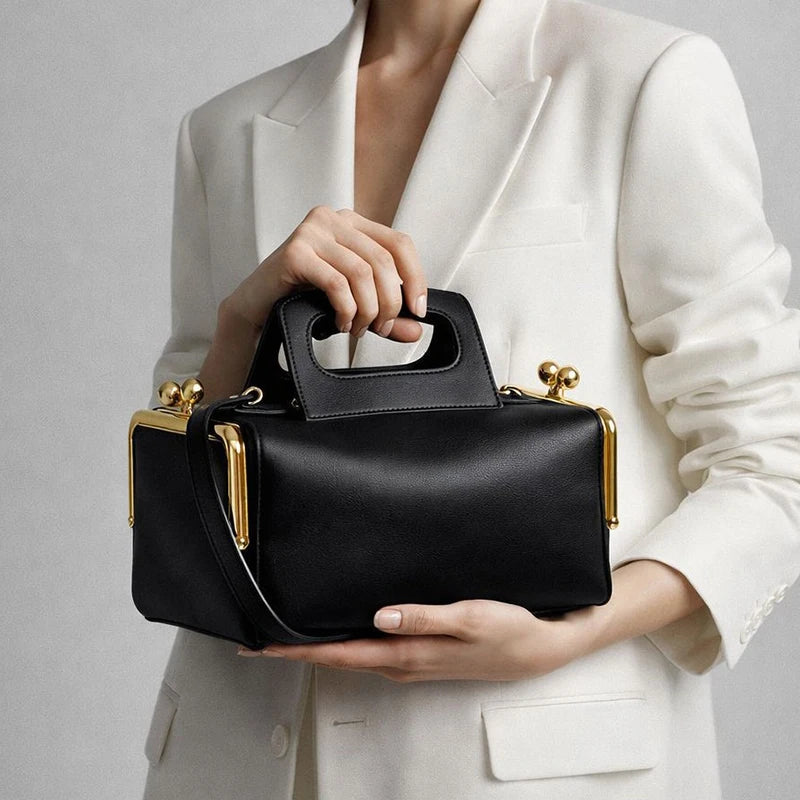 Person holding a black handbag with gold accents against a neutral background